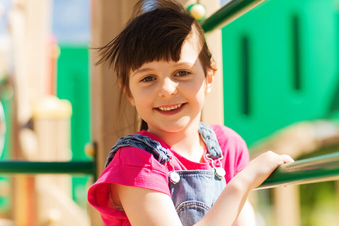 Dark haired girl smiling at camera on playground