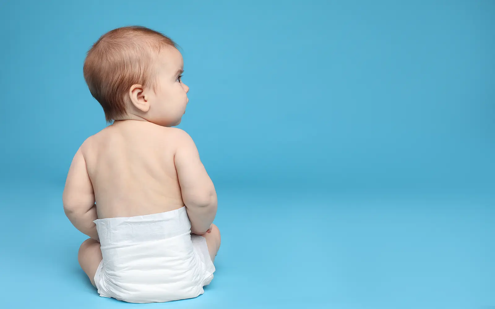 Baby sitting in a diaper against a blue background