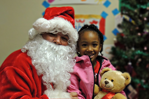 Picture of a pretty young African American girl in pink jacket sitting with volunteer Santa in one of our Kansas City communities