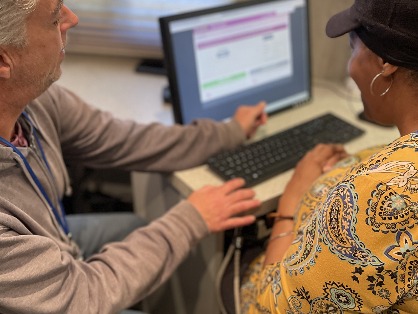 Volunteer pointing at a computer screen while assisting an older adult with an online form.